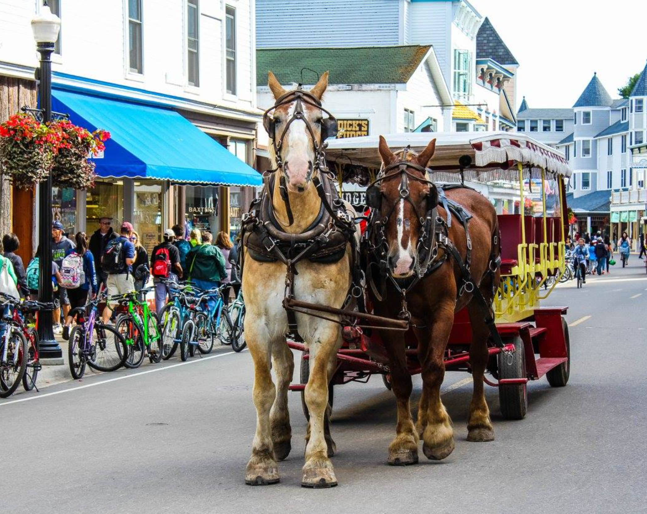 Downtown Mackinac Island with horse-drawn carriages, bicycles, shops, and visitors on Main Street